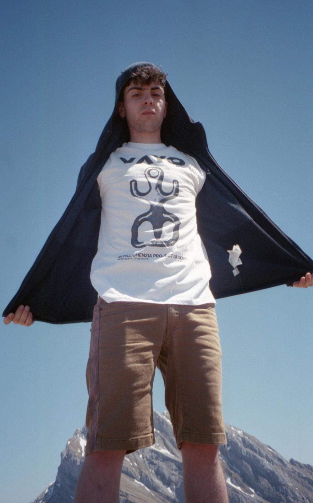 Climber on a mountain summit opening his jacket to reveal a VAYO t-shirt